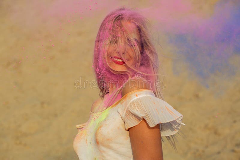 Emotional blonde girl posing in a cloud of pink and blue dry paint Holi at the desert. Emotional blonde woman posing in a cloud of pink and blue dry paint Holi royalty free stock photography